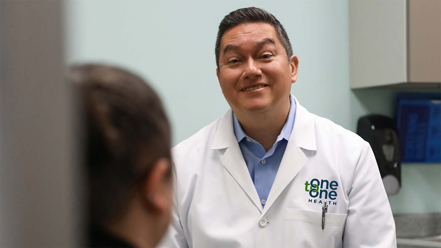 One to One Health provider smiling during a patient consultation in a clinic exam room, reflecting personalized, relationship-based care