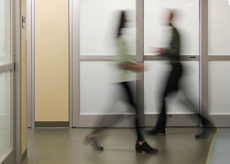 Blurred motion of healthcare staff walking through modern clinic hallway, symbolizing fast, efficient in-person care