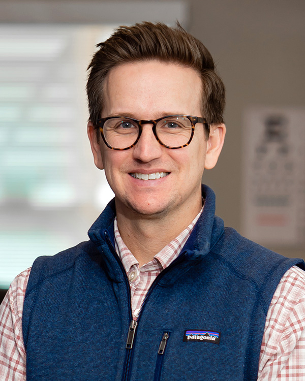 Portrait of Paul Dickenson, Chief Financial Officer at One to One Health, wearing glasses and a blue vest in an office setting