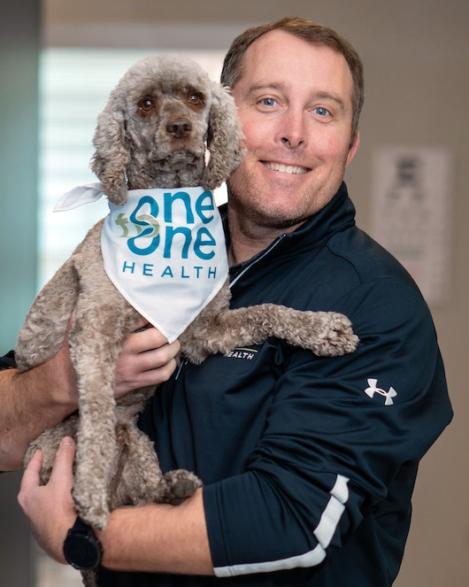 Tillman Endsley, SVP of Operations and Product at One to One Health, smiling while holding a dog wearing a One to One Health bandana